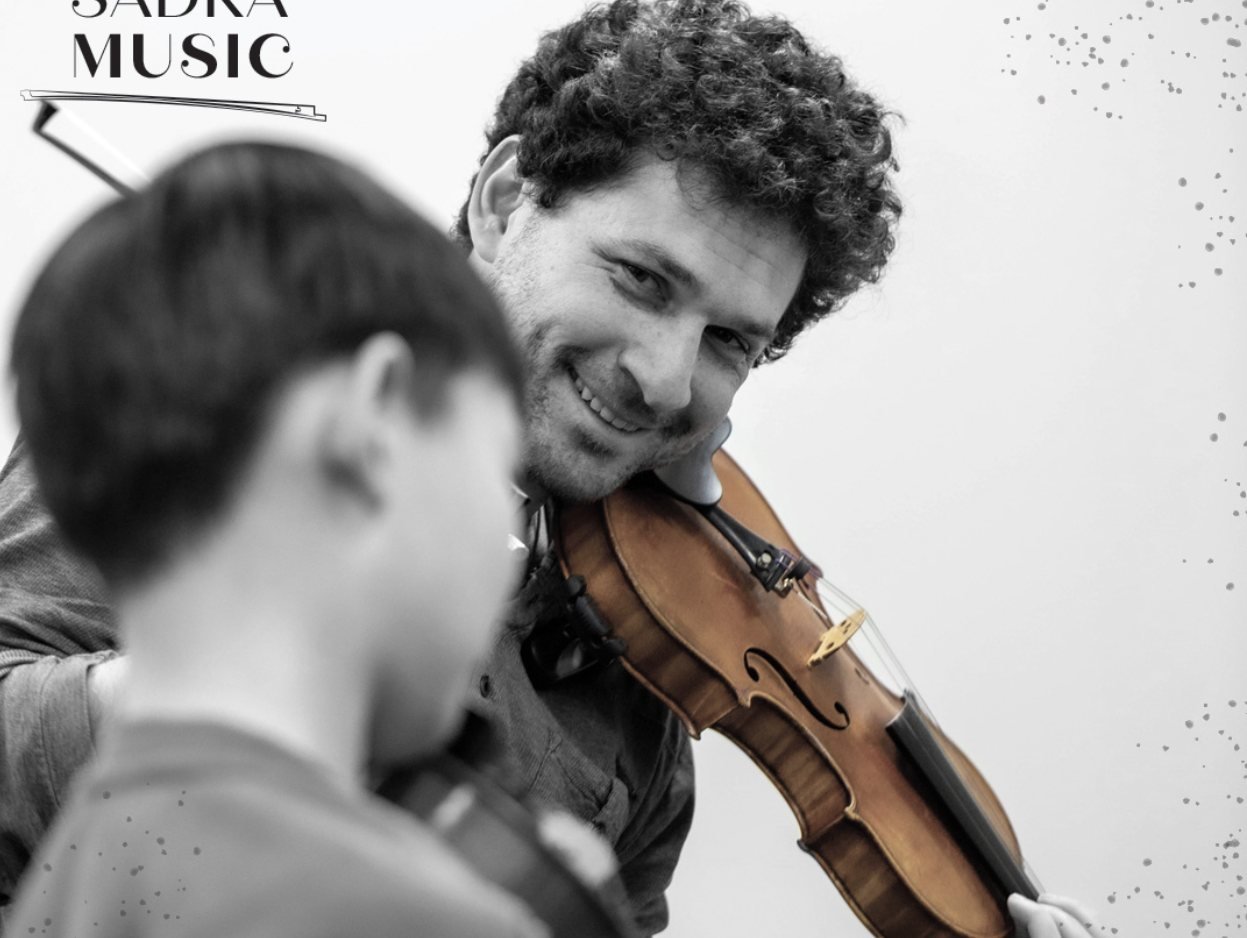Mark Sadka smiling at a young violin student during a lesson, branded with the Sadka Music mark